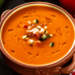 Bowl of tomato soup garnished with herbs.
