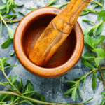 Wooden mortar and pestle with fresh herbs.