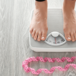 Person standing on a weighing scale with a measuring tape placed around their feet.