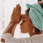 Woman with a green towel on her head and hands in prayer pose.
