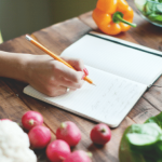 Person writing in a journal with fresh produce around.