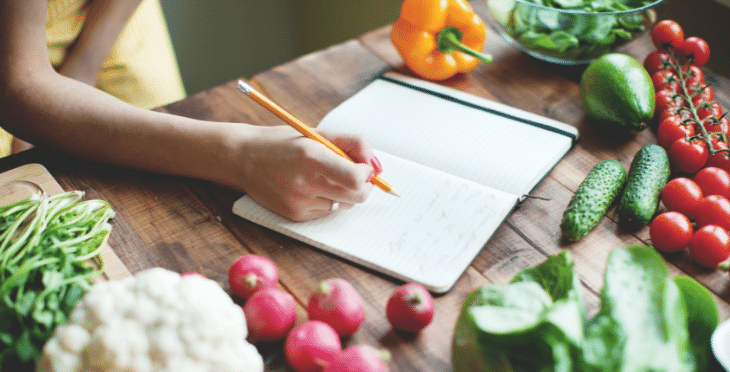 Person writing in a journal with fresh produce around.