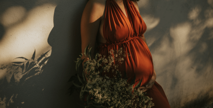 Pregnant woman in a dress holding flowers near her belly.