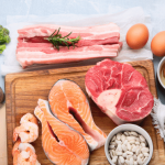 Cutting board with fresh meat, salmon, and eggs ready for meal prep.