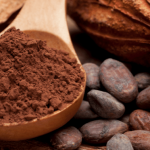 Close-up of a spoon with cocoa powder next to cocoa beans.