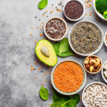 Healthy foods like avocados, seeds, and grains arranged on a table.