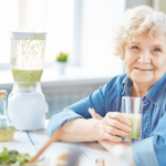 Senior woman smiling with a smoothie and a blender.