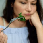 Woman eating a leafy vegetable with contemplation.