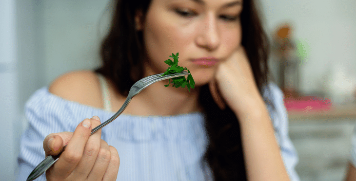 Woman eating a leafy vegetable with contemplation.
