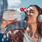 Woman drinking water from a bottle while wearing headphones.