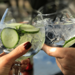 Hands holding glasses of cucumber water.