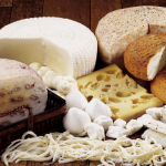 Variety of cheeses with bread on a wooden board.