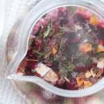 Teapot pouring herbal tea with floating ingredients.