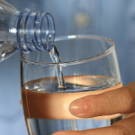 Hand pouring water from a bottle into a glass.