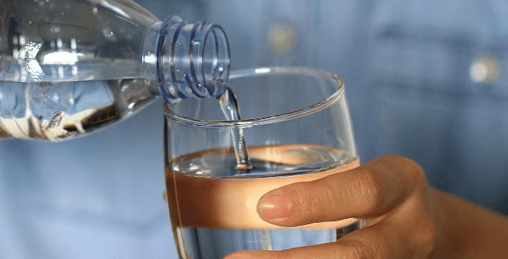 Hand pouring water from a bottle into a glass.