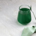 Small glass of green juice on a white surface.