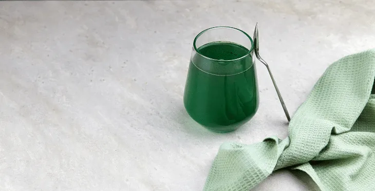 Small glass of green juice on a white surface.