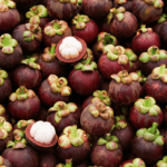 Cluster of fresh mangosteens with one cut open to reveal the white flesh.