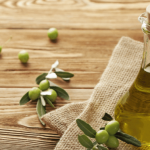 Fresh olives, olive leaves, and a small bottle of olive oil on a wooden surface.
