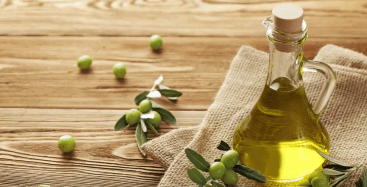 Fresh olives, olive leaves, and a small bottle of olive oil on a wooden surface.