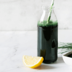 Glass bottle of green juice with a lemon slice on a white background.