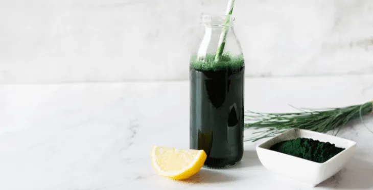 Glass bottle of green juice with a lemon slice on a white background.