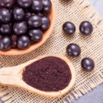 Bowl of black olives with a wooden spoon on a woven mat.