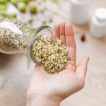Hand holding a jar of hemp seeds with a wooden spoon nearby.