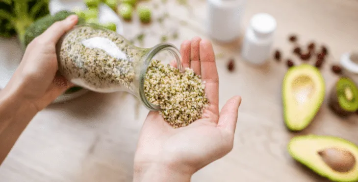 Hand holding a jar of hemp seeds with a wooden spoon nearby.