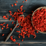 Red goji berries spilling from a spoon onto a dark surface.