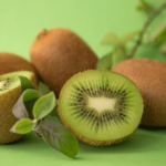 Sliced kiwi fruit with whole kiwis and leaves on a green background.