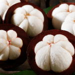 Fresh mangosteen fruits, some cut open to reveal white flesh.