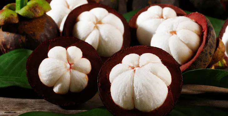 Fresh mangosteen fruits, some cut open to reveal white flesh.