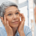 Elderly woman applying cream to her face.