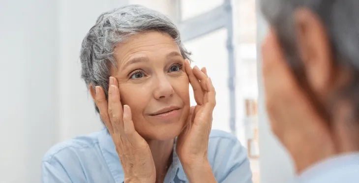 Elderly woman applying cream to her face.