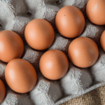 A dozen brown eggs arranged in a gray cardboard egg carton on a burlap surface.