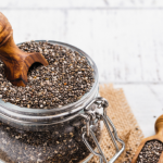 Jar of chia seeds next to a wooden spoon.