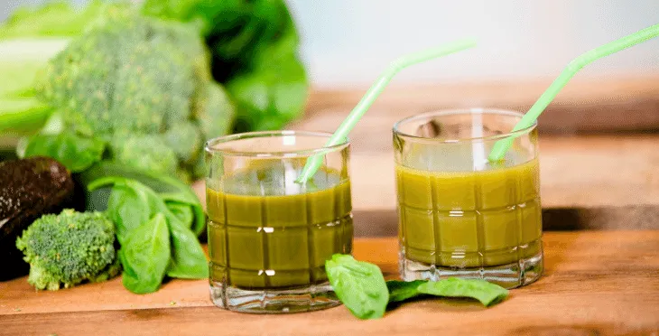 Two glasses of green juice with celery sticks on a wooden surface.