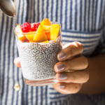 Person holding a glass jar filled with chia pudding topped with fresh fruit.